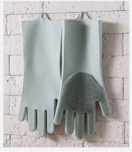 Charger l'image dans la galerie, Gants de vaisselle en silicone avec brosses intégrées suspendus sur un mur en briques blanches.